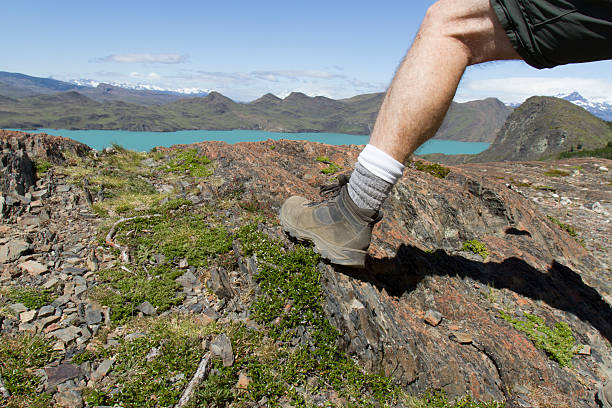 Boots on man standing on overlook of Sapphire Lake in Torres del Paine, Patagonia, Chile on sunny day.