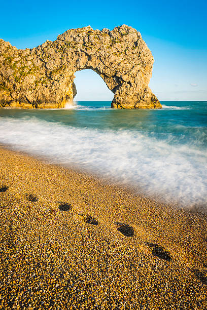 empreintes de pas sur la plage de l'océan bleu surf rock arch blanc - vibrant color summer rock cliff photos et images de collection