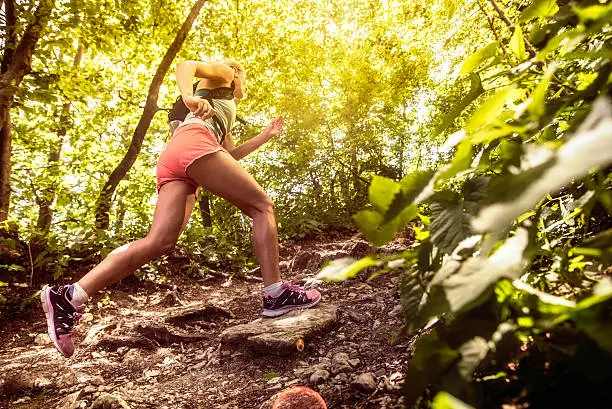 Side view shot of a sports woman running uphill on rough terrain in a forest.