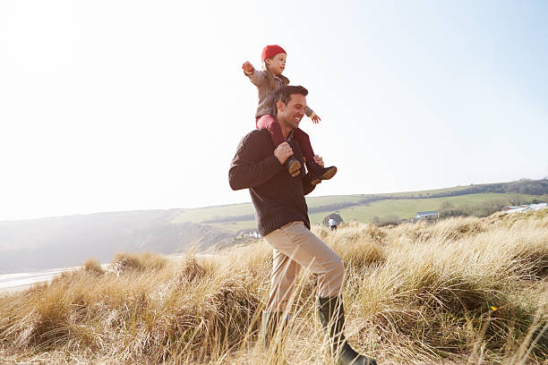 Father And Daughter Walking Through Dunes On Winter Beach