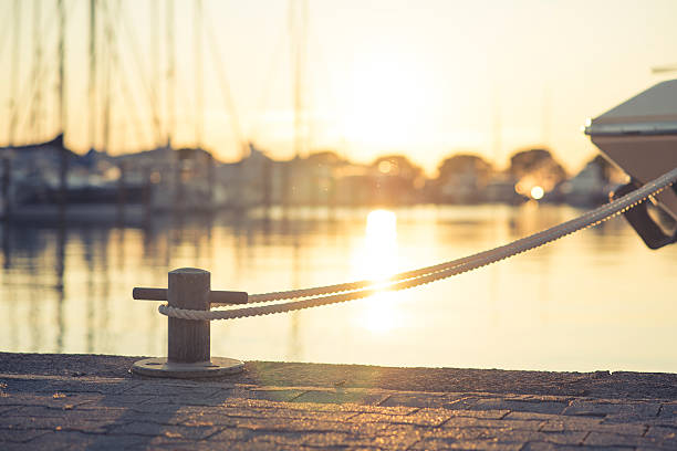 Yacht moored on harbour Yacht in port tied with a rope on mooring post on harbour during sunset. Sun and reflection of it in back. lake boat dock stock pictures, royalty-free photos & images