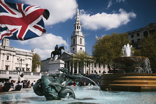 London, United Kingdom - April 14, 2014: Commuters and tourists are sitting around fountains on Trafalgar Square, London. Trafalgar Square is a public  square in the City of Westminster, Central London, built around the area formerly known as Charing Cross.