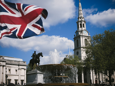 London, United Kingdom - April 14, 2014: Commuters and tourists are sitting around fountains on Trafalgar Square, London. Trafalgar Square is a public  square in the City of Westminster, Central London, built around the area formerly known as Charing Cross.