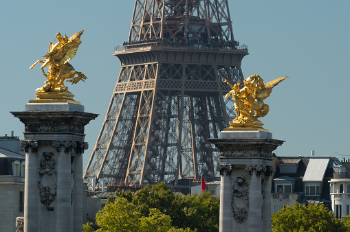 Two pillars of the Pont Alexandre IIIwith golden statues with the Eiffel tower partly visible in the background.
