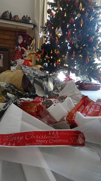Christmas Day mess Close up of the Christmas day wrapping mess with the Christmas tree in the background. christmas chaos stock pictures, royalty-free photos & images