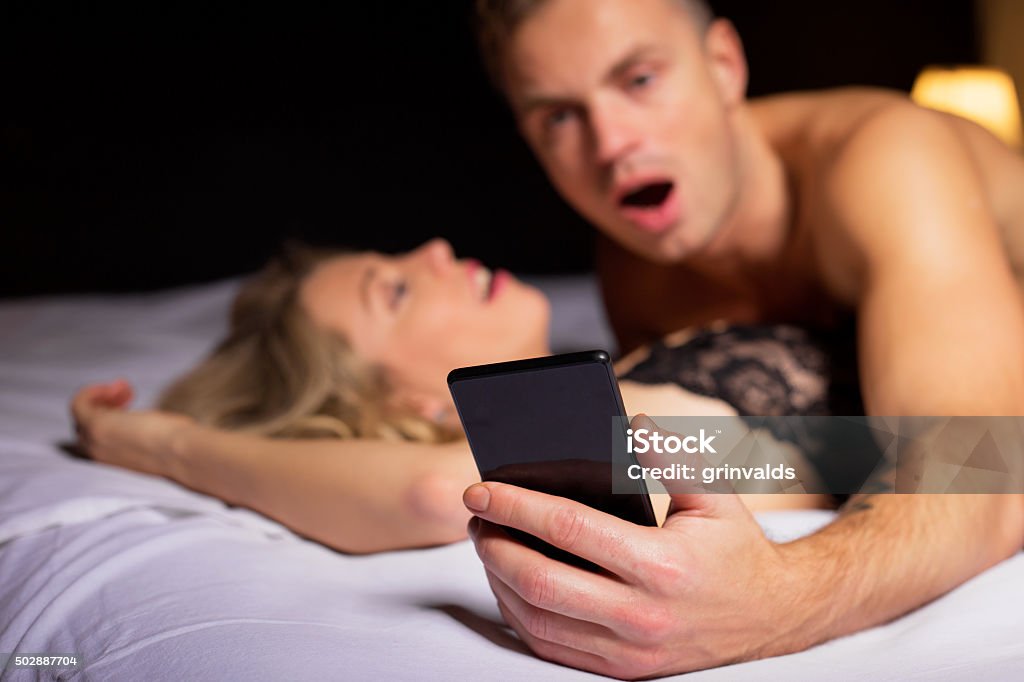 Surprised man looking at his phone Surprised man looking at his phone while laying on top of woman Sex and Reproduction Stock Photo