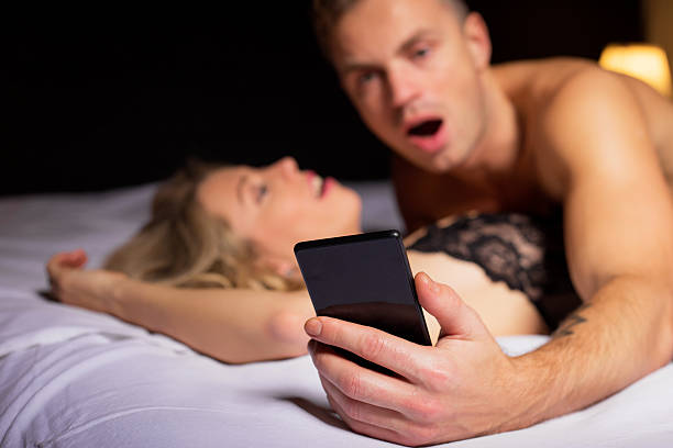 zaskoczony mężczyzna patrząc na jego telefon - sexual activity bed couple young couple zdjęcia i obrazy z banku zdjęć