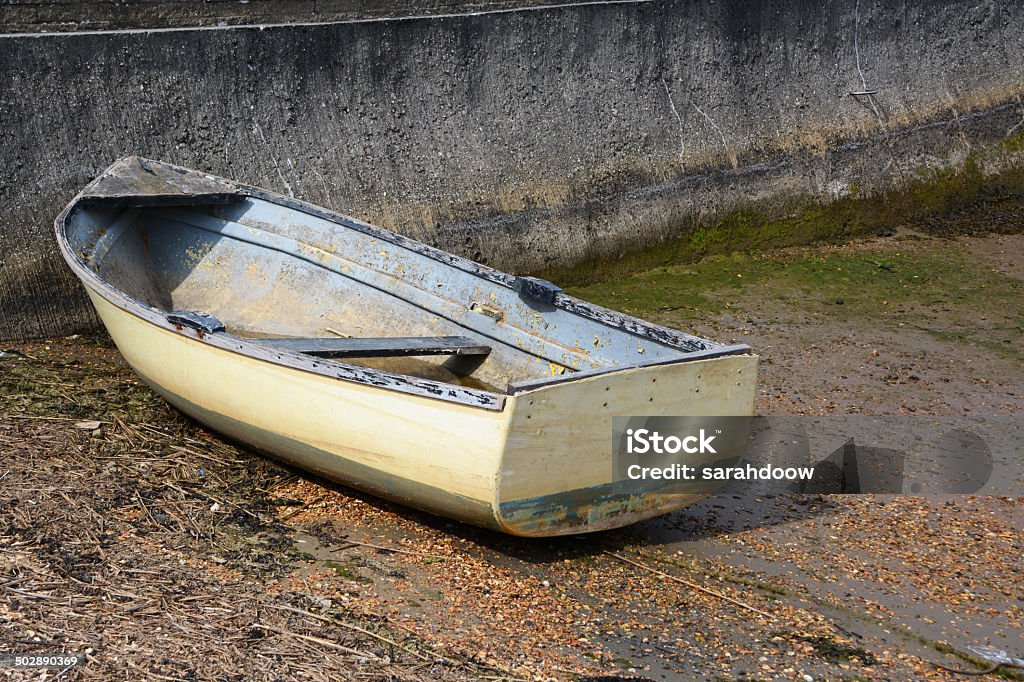 Weather-beaten dinghy on a concrete slipway Weather-beaten white and blue dinghy with peeling paint, out of water on a concrete slipway Abandoned Stock Photo