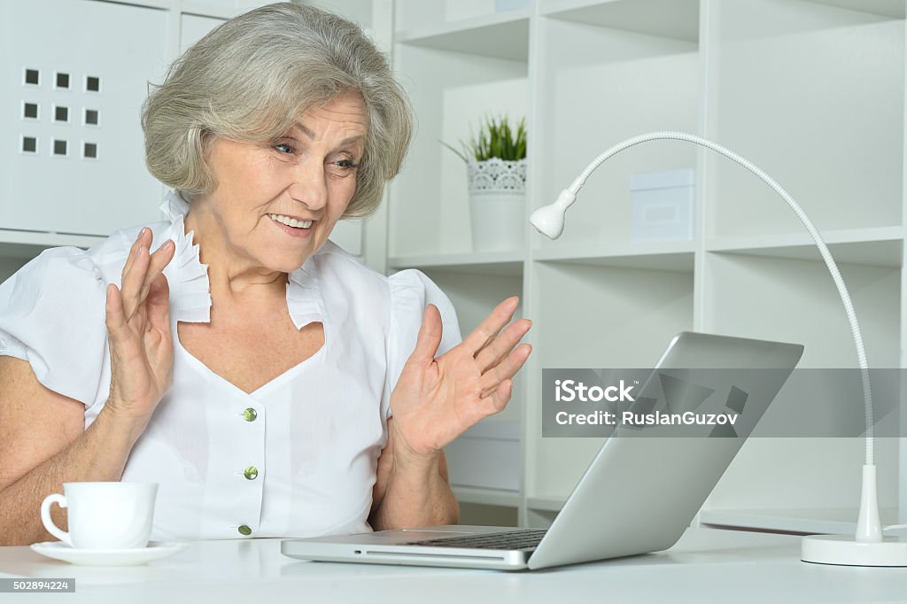 Elderly woman working on laptop surprised Elderly woman working on laptop in office 2015 Stock Photo