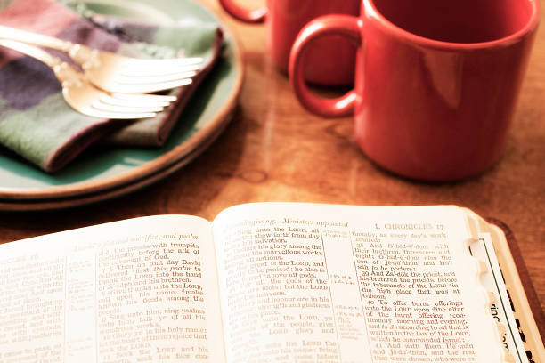 Open Bible with red coffee cups, forks, plates in background. Morning bible study.  
