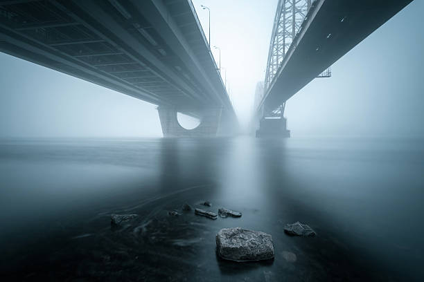 Two parallel bridges over foggy river.