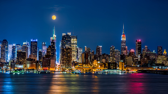 Super Moon above New York skyline. The top of the Empire State Building is illuminated with the colors of the German and Argentinian flags in honor of the Soccer World Cup final.