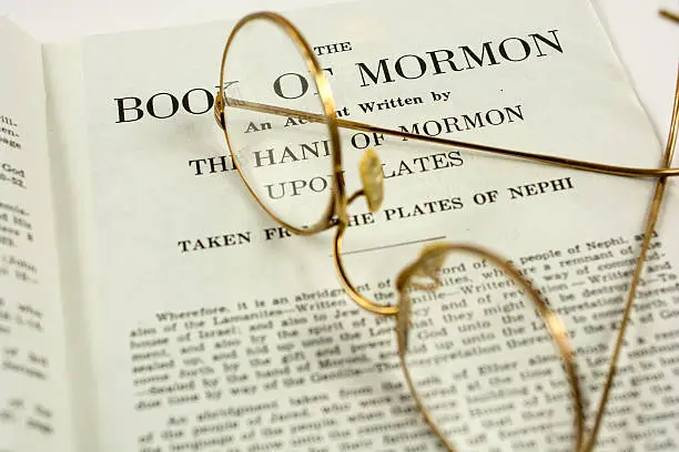 The opening page in the Book of Mormon. A pair of old glasses rests upon the page.
