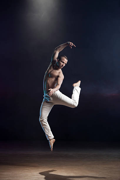 Dance is Power! Young and muscular man performing a contemporary dance pose on a stage. ballerina shadow stock pictures, royalty-free photos & images