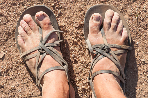Closeup POV of dusty male feet in traditional rustic leather strap sandals standing on dry barren ground