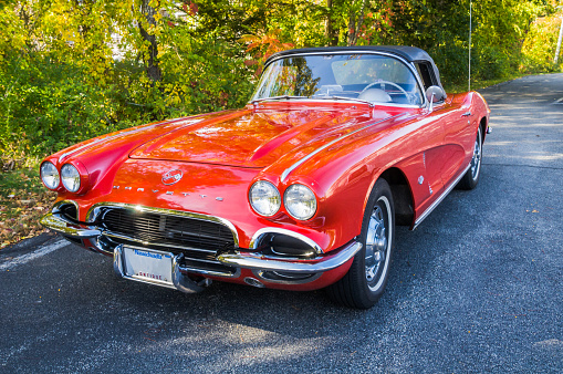 west Barnstable, Massachusetts, USA - October 27, 2015: A well restored and cared for 1962 Red Corvette Convertible, a Chevrolet classic sports car, is parked next to a wooded setting with bright Autumn colors.  .  Property release available.