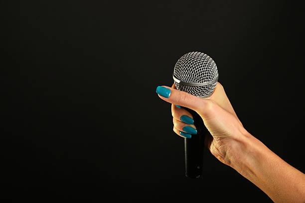 istock Woman hand with microphone isolated on black 502919596