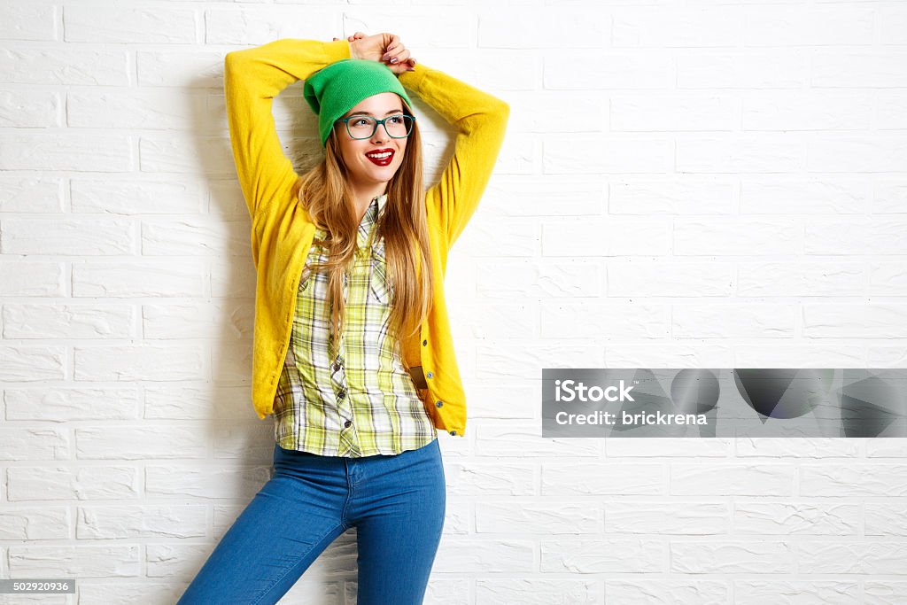 Smiling Hipster Girl at White Brick Wall Background Smiling Hipster Girl at White Brick Wall Background. Street Syle. Trendy Casual Fashion Outfit in Spring or Autumn. Copy Space. Eyeglasses Stock Photo