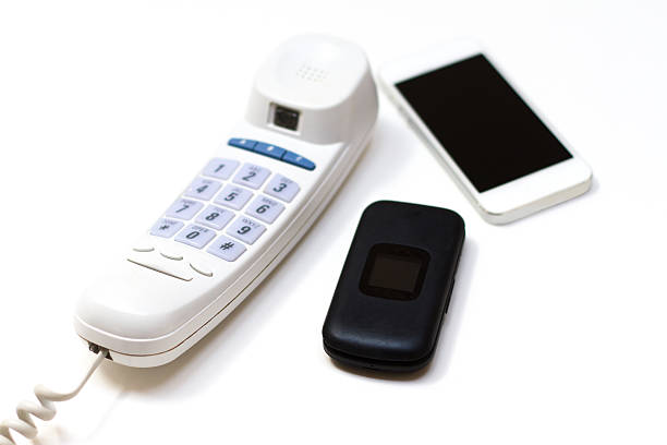 Trio of phones old and new: a corded phone, a flip phone and a smartphone on a white background. Copy space available. Colors are black, white, light blue.