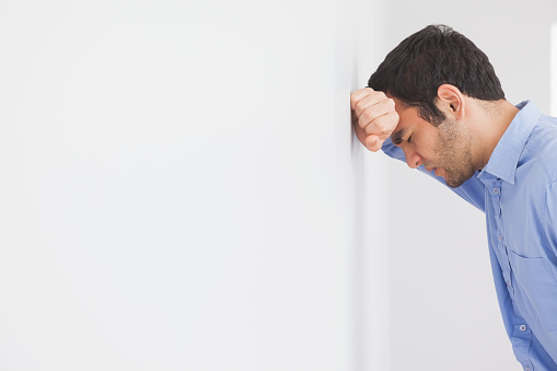 Angry man with fist clenched leaning his head against a wall