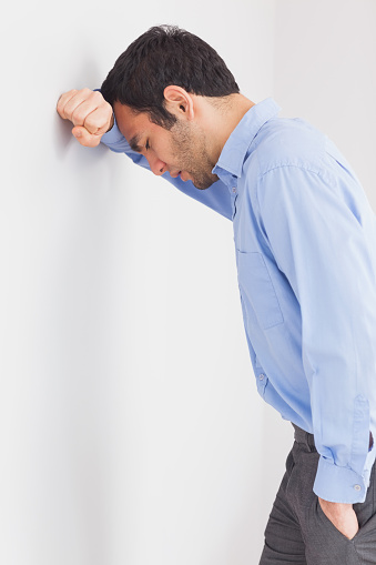 Worried man with fist clenched leaning his head against a wall