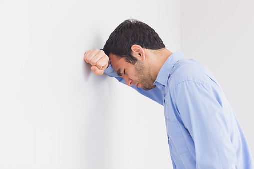 Upset man with fist clenched leaning his head against a wall