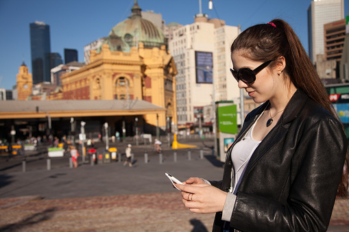 A young woman texting her friends in Federation Square, Melbourne, Australia. Fed Square is in the heart of Melbourne and is a well known meeting point.