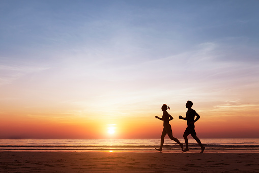 Silhouette of two sportive runners running on the beach at sunset, concept about healthy lifestyle and wellbeing