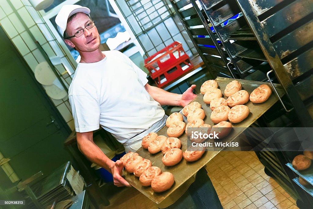 Baker with fresh baked rolls Male baker with fresh baked rolls on a baking sheet. Adult Stock Photo