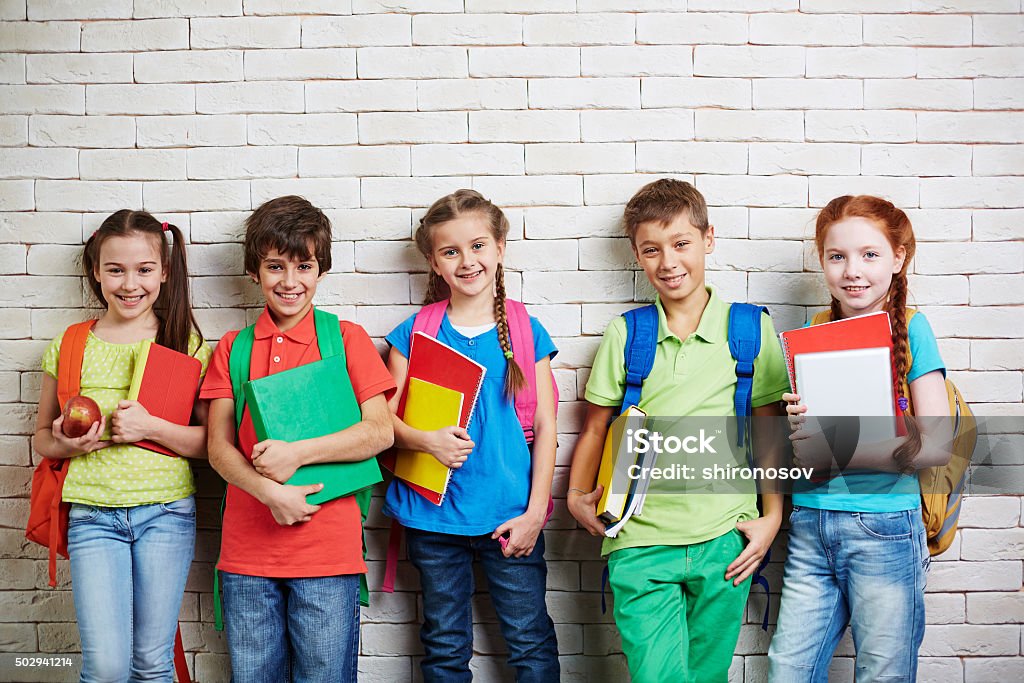 Modern schoolchildren Group of cute schoolkids standing by wall and looking at camera School Children Stock Photo
