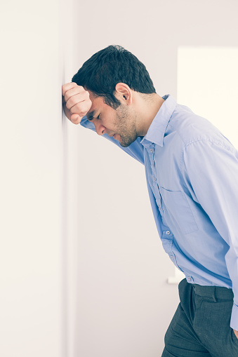 Devastated man with fist clenched leaning his head against a wall