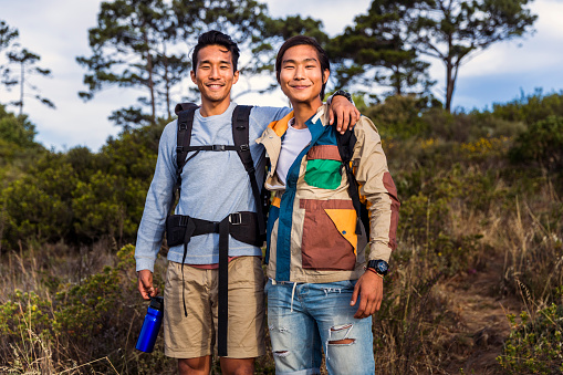 A photo of hikers in forest. Portrait of men are smiling together. Young male is standing arm around friend in woodland during weekends.