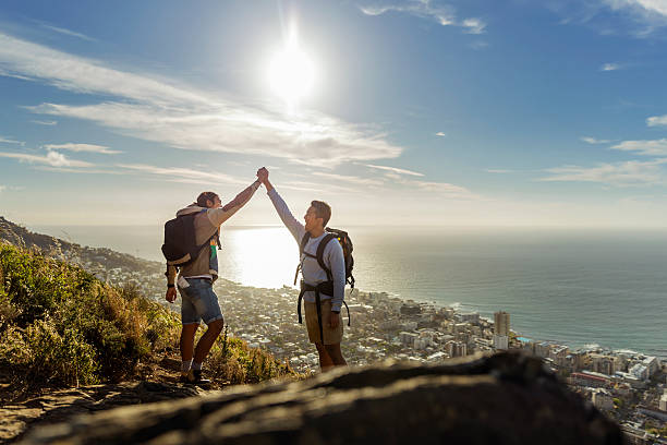 Gay hikers celebrating success on hill A photo of gay hikers celebrating success on hill. Happy couple are holding hands. Full length of young males are in casuals against sky. gay man photos stock pictures, royalty-free photos & images