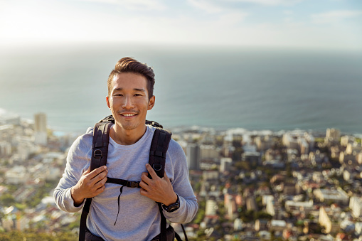 A photo of hiker smiling against sea. He is carrying backpack. Happy male is in casuals. Portrait of young man is enjoying his vacations.
