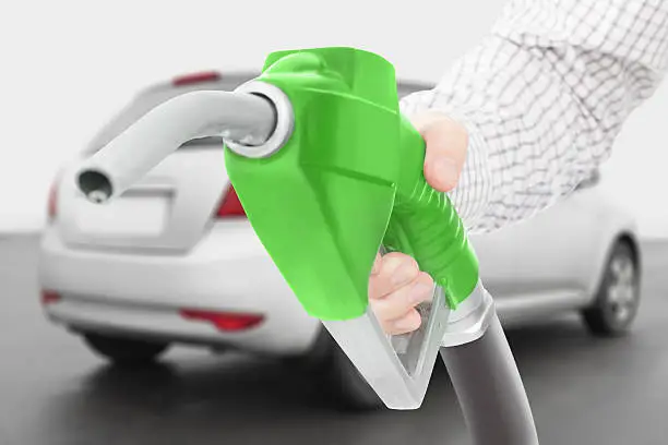 Green color fuel pump gun in hand with car on background