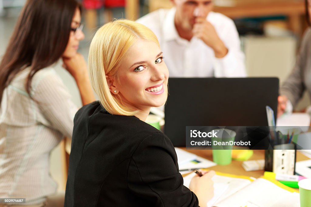 Portrait of a smiling businesswoman Portrait of a smiling businesswoman in office, with her colleagues in background Adult Stock Photo