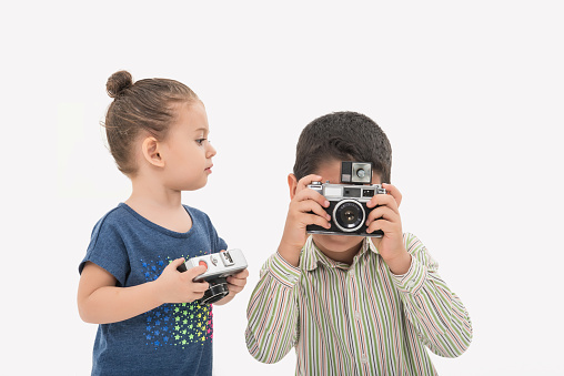 Cute toddler girl taking picture with her brother. Baby girl is 2 years old and the little boy is 7 years old. Image taken in studio over white background. Camera Nikon D800