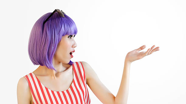 Young woman, profile shot, with violet hair and red dress showing and looking surprisingly at something on the hand , isolated on white background