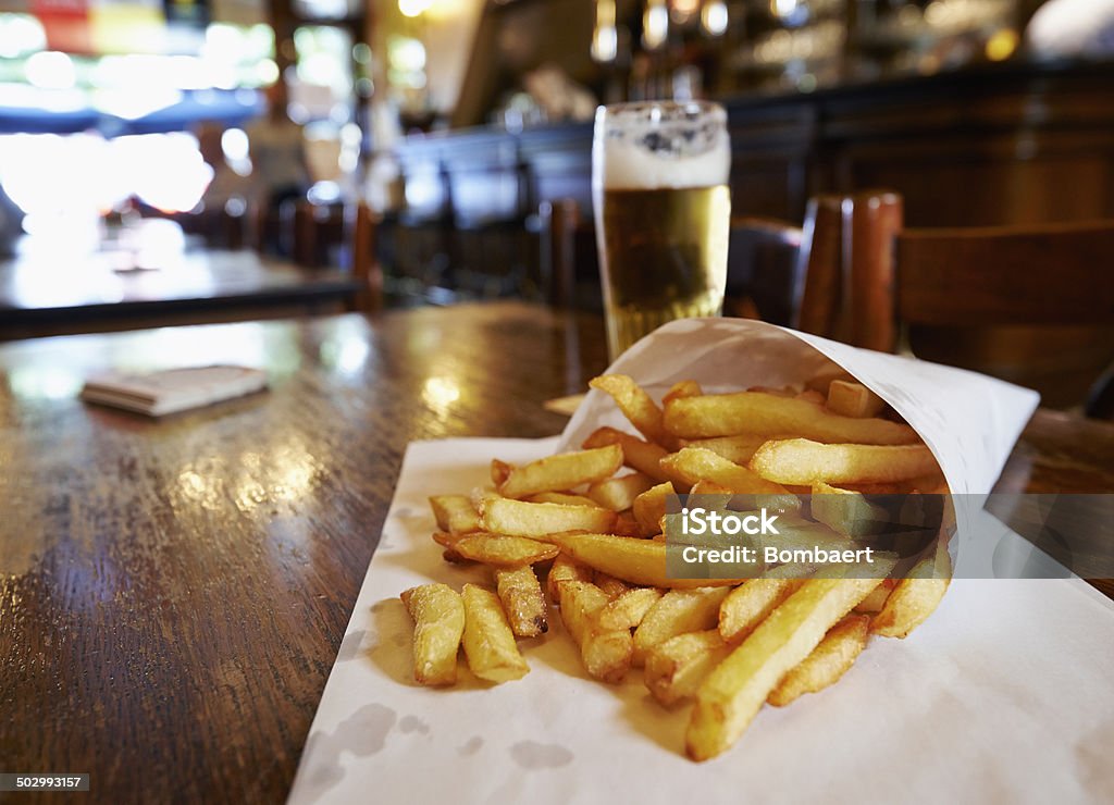 Potatoes fries in a little white paper bag Potatoes fries in a little white paper bag on wood table in brussels pub Beer - Alcohol Stock Photo