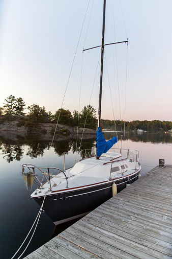 A small sailboat sits docked on a calm lake during the evening.