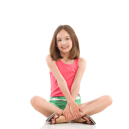 Smiling young girl posing wth legs crossed. Full length studio shot isolated on white.