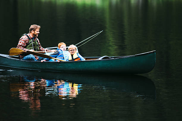 Family Fishing Trip A father takes his two sons on a fly fishing lake trip in the trusty canoe. One of the boys has caught a fish and reels it in for his brother to net. Shot in the beautiful Pacific Northwest at Trillium Lake, Oregon. rowing boat fishing stock pictures, royalty-free photos & images