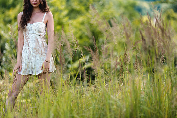 Portrait of a beautiful red-haired girl in a straw hat with meadow flowers, standing in a beautiful meadow at sunset on a summer day.
