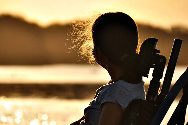 Girl In Wheelchair Teenage girl with cerebral palsy sits in a wheel chair watching the sunset by a river. paraplegic stock pictures, royalty-free photos & images