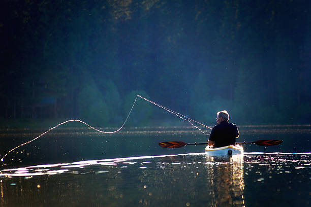 Fishermans Cast on a Sunny Afternoon A fisherman casting on a lake from a kayak, backlit by the afternoon sun rowing boat fishing stock pictures, royalty-free photos & images