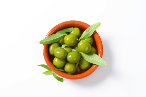 bowl of fresh green olives and leaves on white background