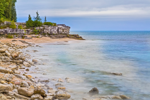 The rocky coast of Cave Point County Park, in Door County, Wisconsin, is photographed with a long exposure under a cloudy morning sky.