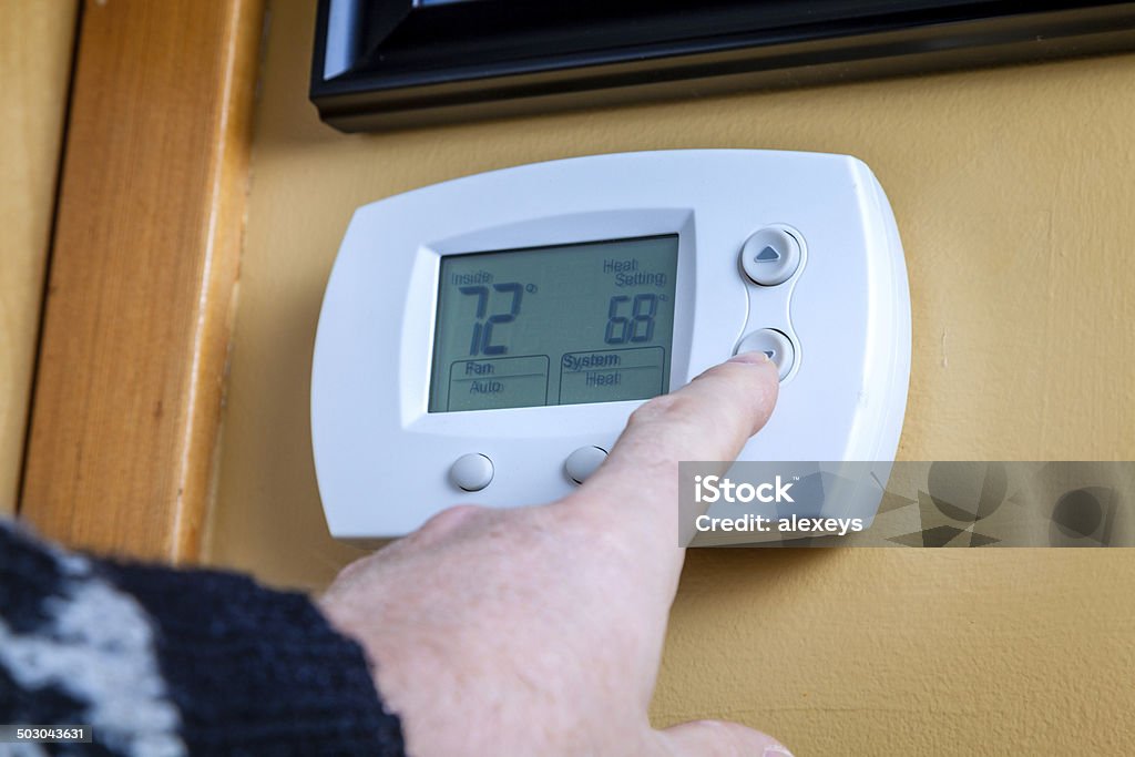 Energy saving A person lowers temperature on a home thermostat. Enegry saving concept Thermostat Stock Photo