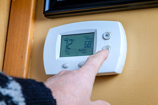 Energy saving A person lowers temperature on a home thermostat. Enegry saving concept thermostat stock pictures, royalty-free photos & images