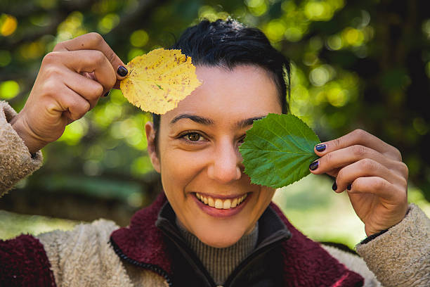 Woman covering face with orange autumn leaves.